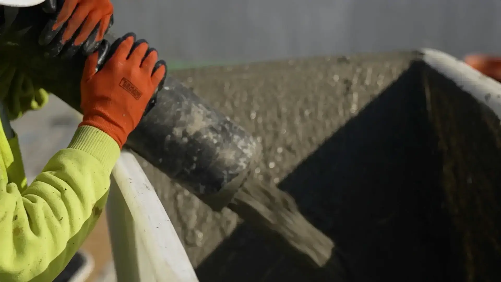 Close-up of a construction worker guiding a concrete hose, pouring fresh mix into a container during a parking garage restoration project